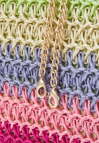 Sac tissé multicolore avec des brins verts, jaunes, violets et roses. Doté de bretelles en chaîne dorée avec fermoirs en forme de homard. Fini texturé.