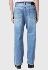 Jeans din denim de culoare albastru deschis, cu un design cu picioare drepte, având buzunare la spate și un etichetă neagră la talie, prezentate din spate.