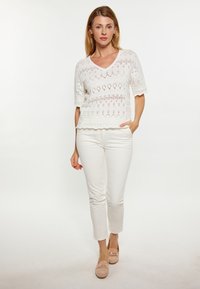 Top bianco a maglia con scollatura a V e maniche corte, caratterizzato da un motivo testurizzato. Abbinato a pantaloni bianchi a gamba dritta e scarpe beige.