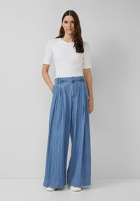 Laiad sinised denim püksid kõrge vöökohaga, pleatidega ja vöödiga. Kombineeritud vormikas valge lühikeste varrukatega topi ja valgete tennistega.