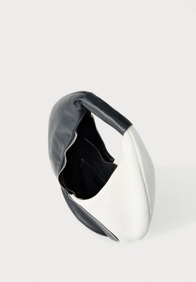 Δίχρωμη δερμάτινη τσάντα χειρός σε μαύρο και λευκό με φαρδιά λαβή και ανοιχτό φερμουάρ που αποκαλύπτει το εσωτερικό από μαύρο ύφασμα.