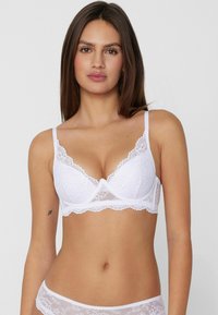 Reggiseno bianco in pizzo con scollatura profonda, bordi smerlati, spalline regolabili e inserti in rete trasparente per un dettaglio aggiuntivo.