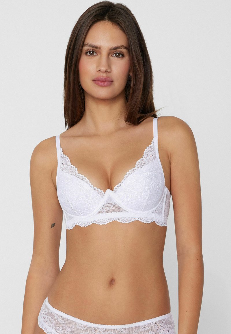 Soutien-gorge en dentelle blanche avec décolleté plongeant, bordures festonnées, bretelles réglables et empiècements en tulle transparent pour plus de détails.
