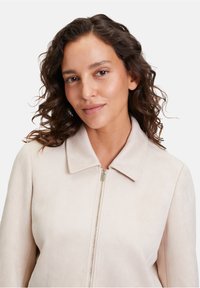 Ljust beige zip-up jacka med krage och mjuk mockakänsla. Har en enkel design utan synliga dekorationer.