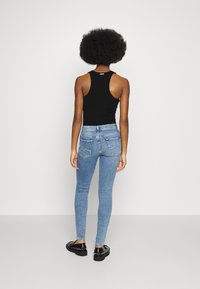 Top sin mangas negro combinado con jeans ajustados azul claro. Los jeans tienen un aspecto desgastado y bolsillos traseros. Unos zapatos negros completan el conjunto.