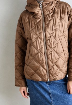 Ruskea tikattu takki, jossa etuvetoketju ja huppu, päällä harmaa neule, yhdistetty siniseen farkkuhameeseen.