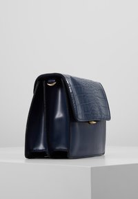 Borsa in pelle blu navy con una patta imbossata a forma di coccodrillo, dotata di una chiusura in oro lucido e due scomparti spaziosi.