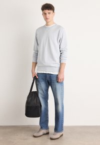 Sudadera de cuello redondo gris claro con un branding sutil, jeans de denim azul y zapatos de color claro; llevando una bolsa de tela negra con un asa corta.