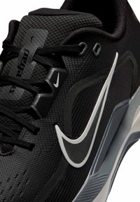 Κοντινή λήψη μαύρου αθλητικού παπουτσιού Nike με λευκό λογότυπο Swoosh, υφασμένο πάνω μέρος, μαύρα κορδόνια και γκρι και λευκές λεπτομέρειες στη σόλα.