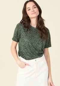 Camiseta de manga corta con estampado de leopardo verde y cuello redondo, combinada con una falda blanca de cintura alta. Tejido suave con un ajuste relajado.