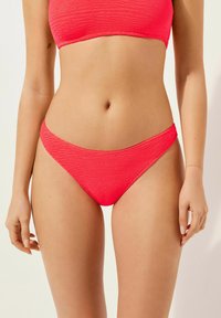 Ljusrosa bikini, texturerad väv med ribbat mönster. Har en åtsittande bandeauöverdel och låg midja, vilket framhäver en enkel stil.
