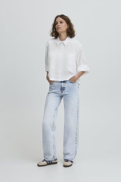 Bijela skraćena košulja s velikim ovratnikom i prednjim džepovima, uparena s širokim svijetloplavim trapericama. Ležerna obuća s tamnim vezicama.