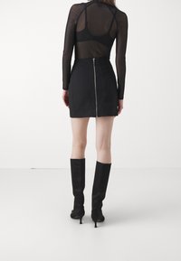 Svart minikjol med dragkedja bak, kombinerad med en genomskinlig långärmad topp. Skor: knähöga svarta stövlar med klack.