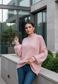 Oversized różowy sweter z dzianiny z wysokim, żeberkowym kołnierzem i balonowymi rękawami, w połączeniu z niebieskimi dżinsami. Gładka tekstura i luźny krój.