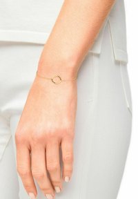 Bracciale d'oro con una catena sottile e un pendente circolare. La catena è delicata e il pendente ha una superficie liscia.