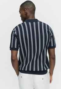 Marinblå pikétröja med kort ärm och vita vertikala ränder, ribbad krage och nederkant; tillverkad av ett mjukt, lätt material.