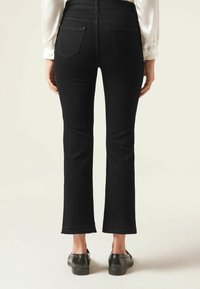 Svarta denimbrallor med utsvängd nederdel och medelhög midja, har två bakfickor och råa nederkanter. I kombination med svarta skor, sedd bakifrån.