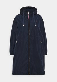 Mørkeblå hætteparka i letvægtsmateriale med fuld lynlås, elastiske manschetter og frontlommer med lynlås. Reflekterende accenter er synlige.