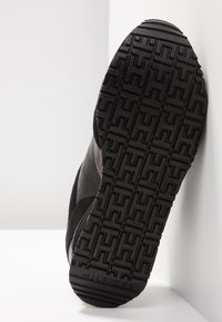 Baskets noires avec une semelle en caoutchouc texturée, dotées d'accents en suède et en matériau lisse, d'un logo embossé, et d'un motif géométrique de la semelle.