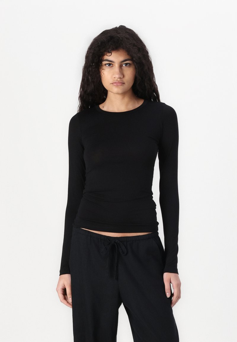 Crni dugouhi prilagođeni top napravljen od mekog materijala, s okruglim izrezom i glatkom teksturom, uparen s labavim crnim hlačama.