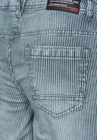 Randiga jeans i ljusblått med en bakficka med sydd detalj och en märkesetikett vid midjebandet, tillverkade av denim.