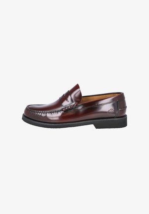 Mocasín tipo penny loafer de cuero marrón oscuro pulido, con suela negra, costura moc toe y pequeño logo en relieve en el lateral del talón.