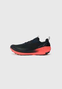 Chaussure de course noire avec un dessus texturé, une semelle rose et un motif de grip prononcé. Présente un tirant et des accents colorés.