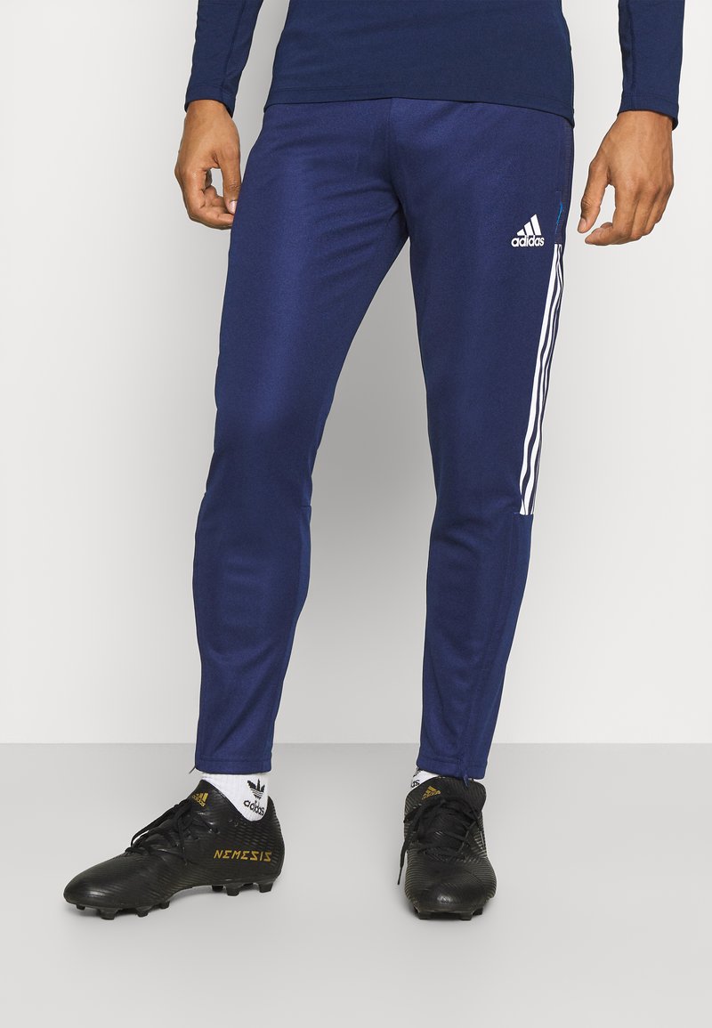 Marineblauwe sportbroeken met drie witte verticale strepen aan de zijkant, gecombineerd met zwarte voetbalschoenen met gouden accenten en logo.