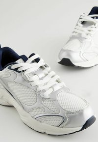 Scarpe da ginnastica bianche con tomaia in rete, dettagli in blu navy, punta rotonda, collo imbottito e suola in gomma. Presentano dettagli a motivo lineare sui lati.
