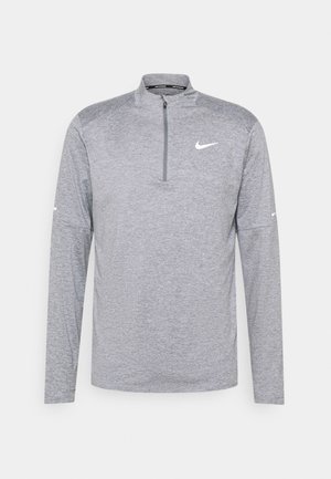 Harmaa pitkähihainen paita, jossa on puolivetoketjukaulus, valmistettu tekstuurikankaasta. Paidassa on valkoinen Nike-logo rinnassa ja hihoissa.