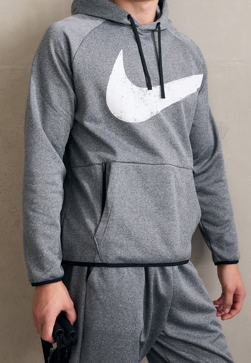 Sweat à capuche gris en tissu doux avec un grand logo Nike blanc. Comprend une poche avant, des cordons de serrage et des poignets côtelés.