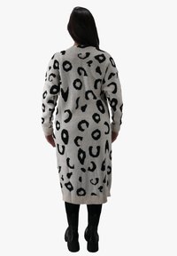 Abito lungo in maglia grigio chiaro con fantasia animalier nera. Caratterizzato da maniche lunghe e orlo a costine. Indossato sopra leggings neri e stivali.