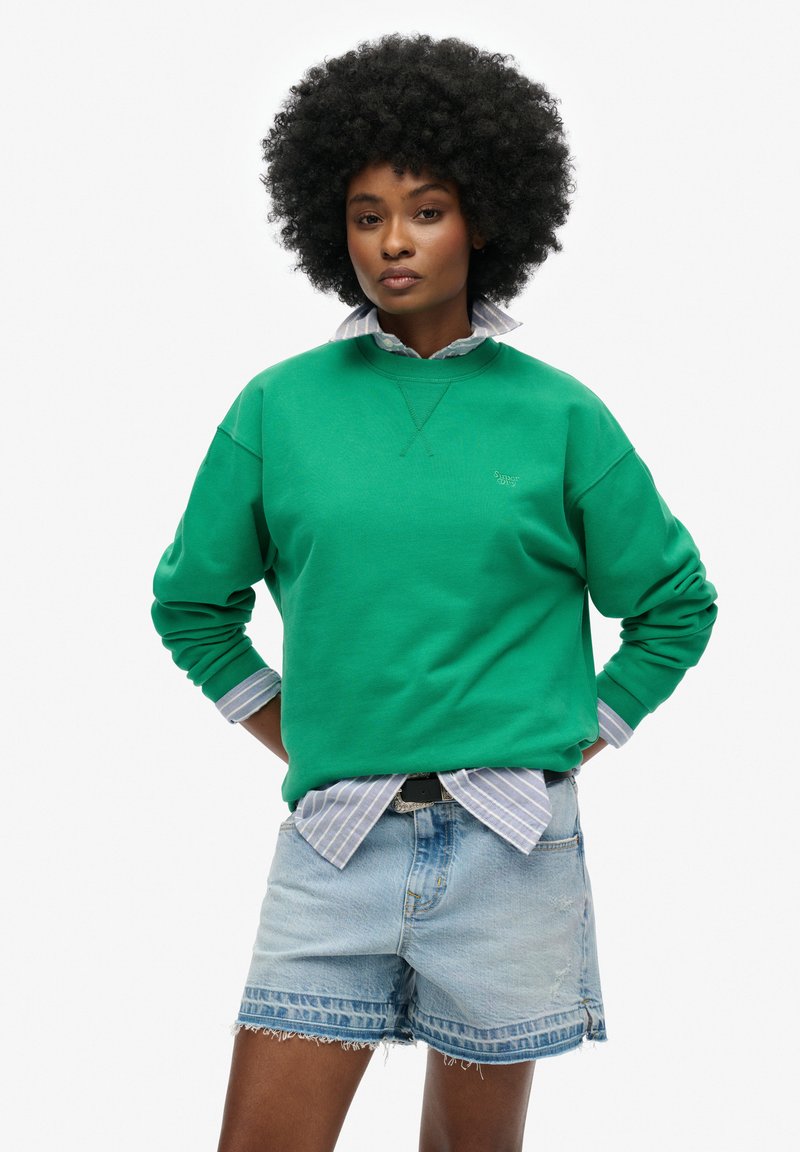 Groene sweatshirt met een ronde hals, lange mouwen en geribbelde manchetten, gelaagd over een lichtblauw gestreept shirt, gecombineerd met denim shorts.