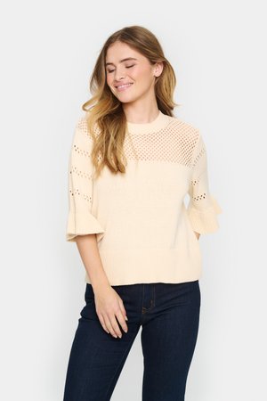 Licht beige gebreide trui met opengewerkte details, geribbelde zoom en uitgewaaierde mouwen. Glad materiaal met een ontspannen pasvorm. Gecombineerd met donkere jeans.
