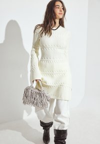 Krēmveida ribota adīta kleita, garas piedurknes, līdz ceļiem. Gaiši pelēks frizēts rokassomu, kombinēta ar baltām biksēm un melniem augstiem zābakiem.