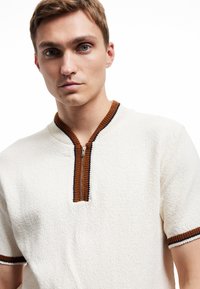 Off-White Kurzarm-Pullover mit braunem und marineblauem geripptem Kragen und Reißverschluss, aus strukturiertem Stoff mit kontrastierenden Besätzen.