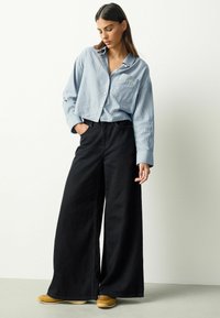 Modrá a biela prúžkovaná košeľa na gombíky s náprsným vreckom; kombinovaná so širokými čiernymi nohavicami a hnedými topánkami. Hladká tkanina a voľný strih.
