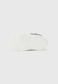 Baskets de sport noires avec une tige texturée, un design à lacets et une semelle extérieure en caoutchouc blanche avec des motifs de traction circulaires.