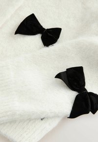 Weißer, strukturierter Stoff mit zwei schwarzen Samtbögen. Die Bögen sind asymmetrisch auf dem Material platziert und verleihen der weichen Oberfläche einen Kontrast.