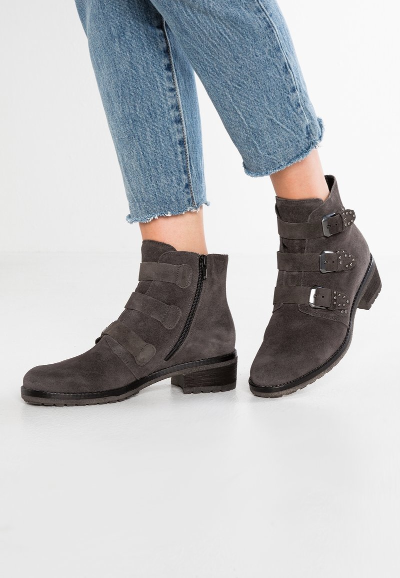 Bottines en daim gris avec trois brides horizontales et détails métalliques, dotées d'une fermeture éclair latérale et d'un talon bas empilé.