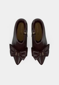 Burgundinės odinės aulinukės, su smailiu kaklu, dekoruotos dideliu kaspinu ir metalinėmis detalėmis, lygia tekstūra ir zip užtrauktuku.