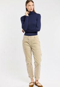 Un pull col roulé marine, un pantalon beige avec des poches et des ballerines marron. Le pull est ajusté ; le pantalon est à coupe décontractée avec des ourlets retroussés.