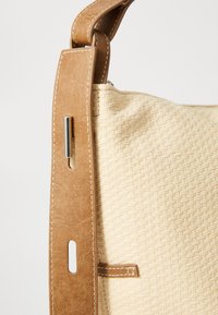 Woven beige handbag featuring a textured body, brown leather strap, and metal hardware accent for adjustable length.