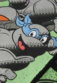 Kreskówkowa postać żółwia z niebieską opaską na głowie i uśmiechniętą twarzą, na zielonym tle z teksturą w kropki.