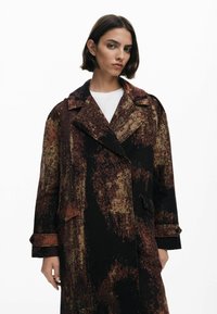 Trench-coat à motif sombre avec un design texturé dans des tons de marron, orange et noir, doté d'un col cranté et de poches avant.