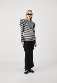 Camiseta de rayas blancas y negras de manga larga con hombros con volantes, combinada con una elegante falda maxi negra y zapatos planos negros.