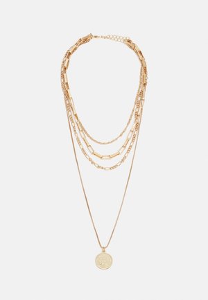 Collier superposé en ton or avec quatre chaînes distinctes, dont une fine chaîne ornée d'un pendentif pièce ronde avec une gravure de profil.