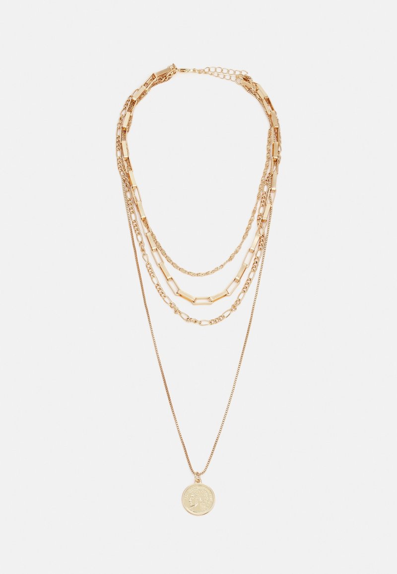Collier superposé en ton or avec quatre chaînes distinctes, dont une fine chaîne ornée d'un pendentif pièce ronde avec une gravure de profil.