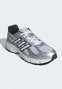 Strieborná a biela bežecká obuv s priedušným zvrškom, syntetickými akcentmi, gumovou podrážkou a tromi čiernymi pruhmi na boku. Ľahký dizajn.