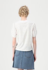 Witte top met pofmouwen van broderie anglaise-textuur, met een ronde halslijn en subtiele scalloped randen. Gekleed met een denim rok.